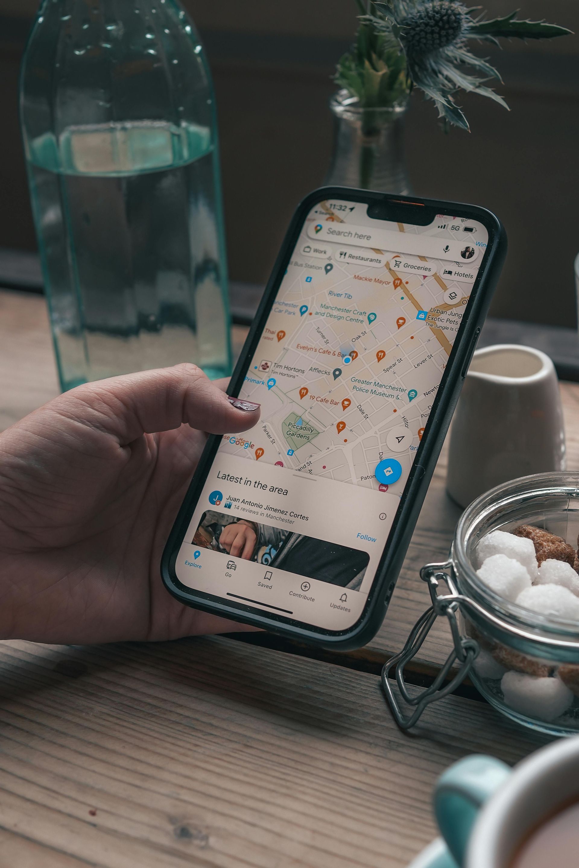 Person using a smartphone with a map app on a wooden table, next to a water bottle and coffee.