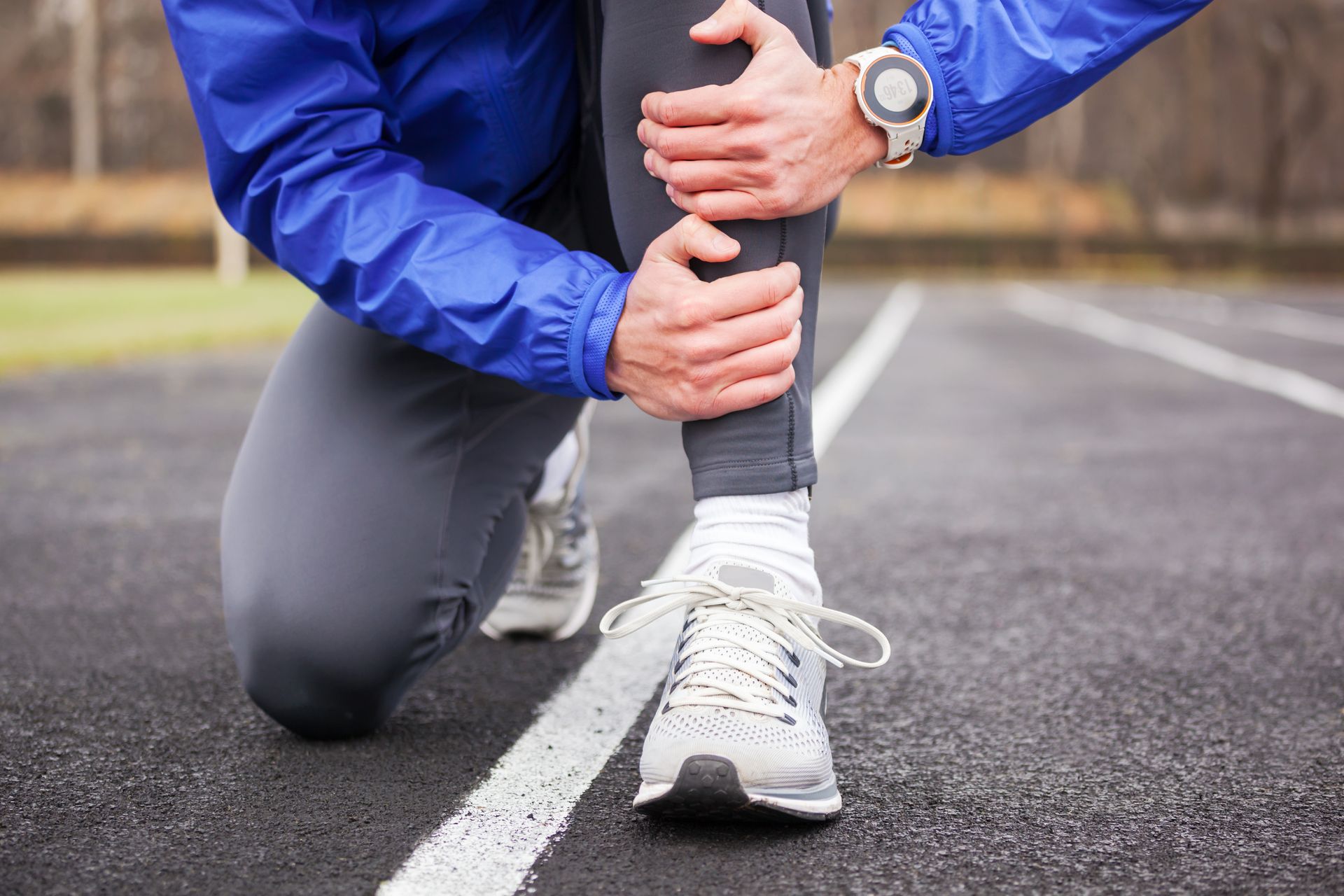 Runner on track clutches their injured leg, likely experiencing pain.