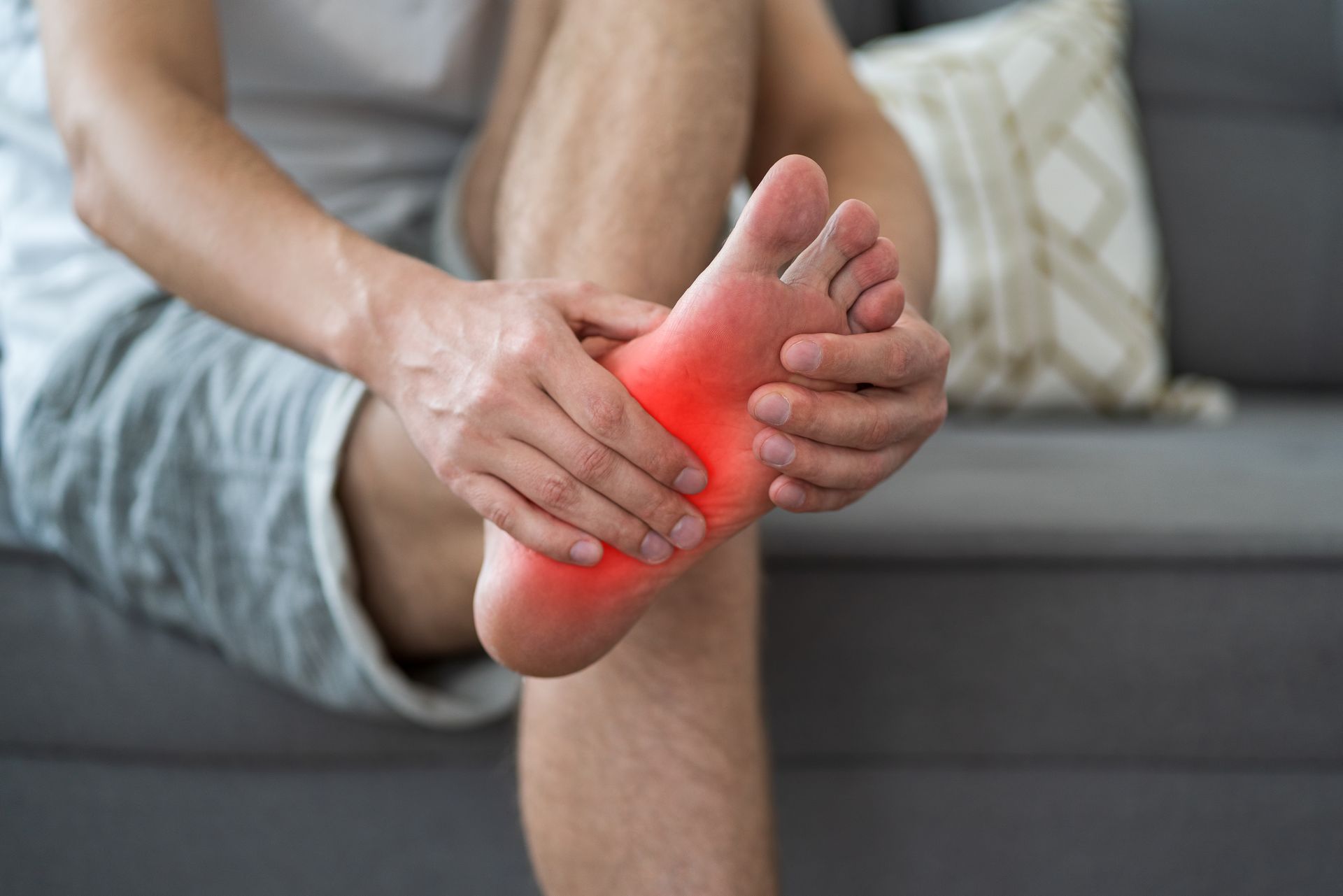 Man holding foot, which is highlighted red to indicate pain. He's sitting on a couch.
