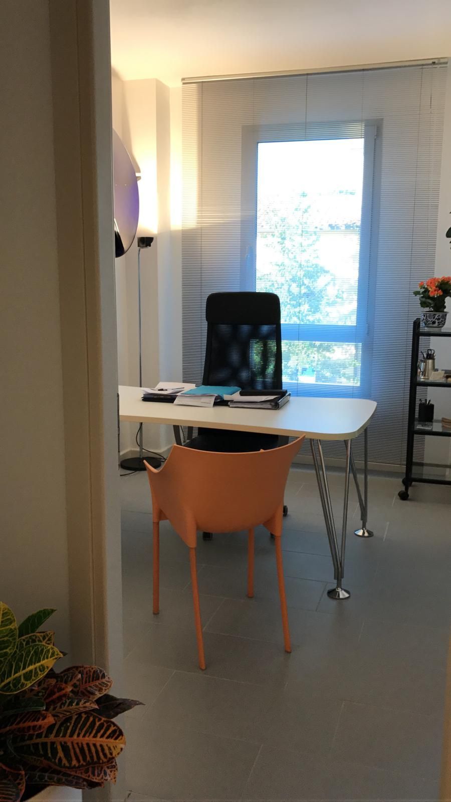 Ufficio con scrivania, sedia arancione, sedia da ufficio nera, finestra e scaffalatura.