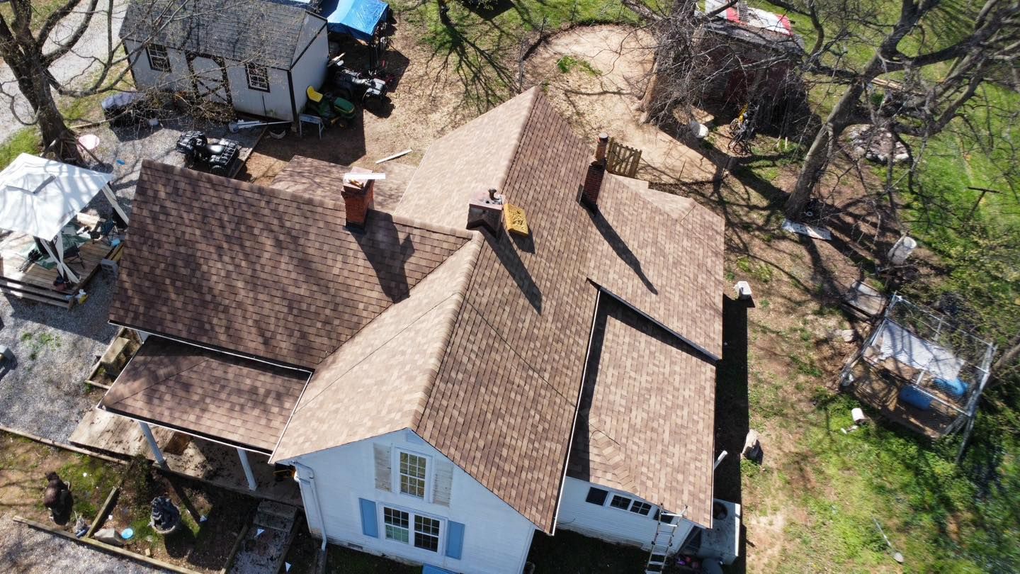 Aerial view of a brown-shingled roof on a white house with trees in the yard.