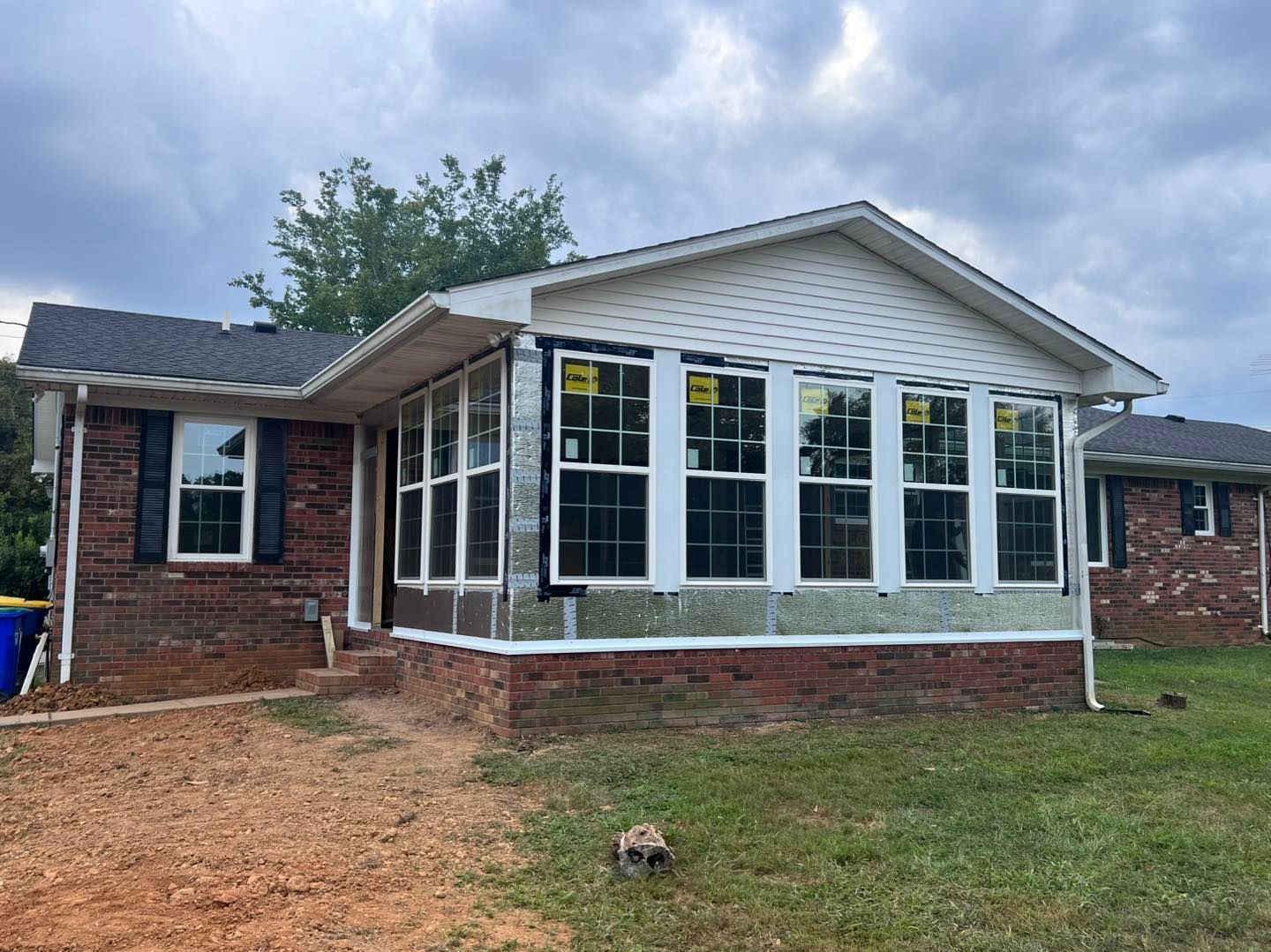 House exterior under construction; brick, siding, large windows, cloudy sky.