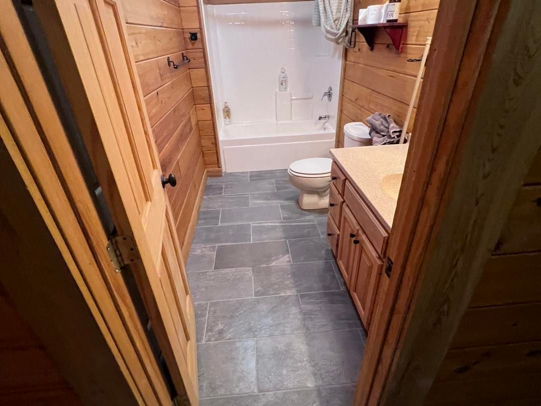 Bathroom with wood paneling, gray tiled floor, white fixtures. Doorways frame the view.