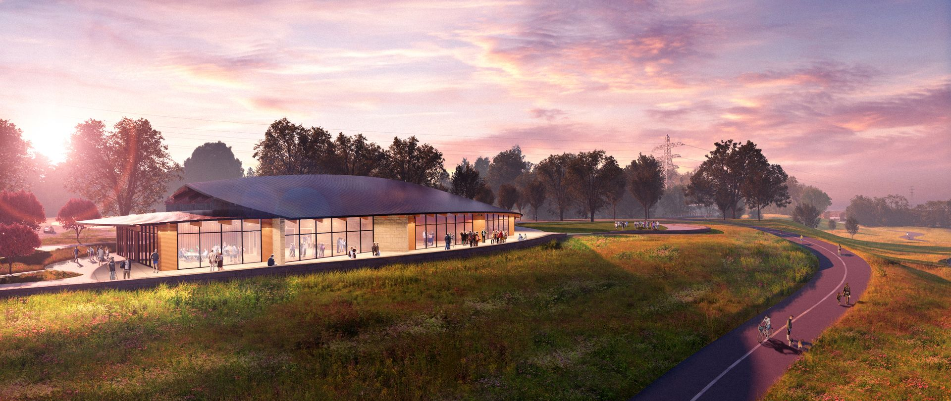 Modern building with glass walls, set in a field with a winding road at sunset.