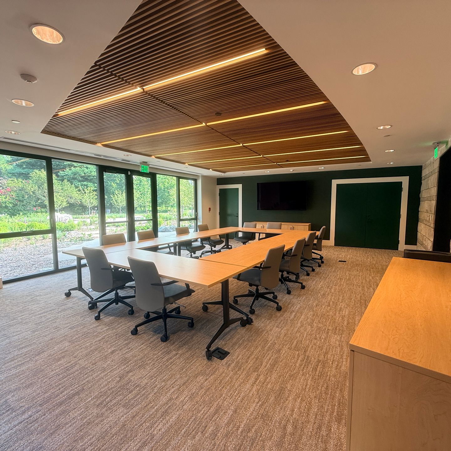 Meeting room with people seated around a long white table, looking at a screen. Large windows for a planning session.