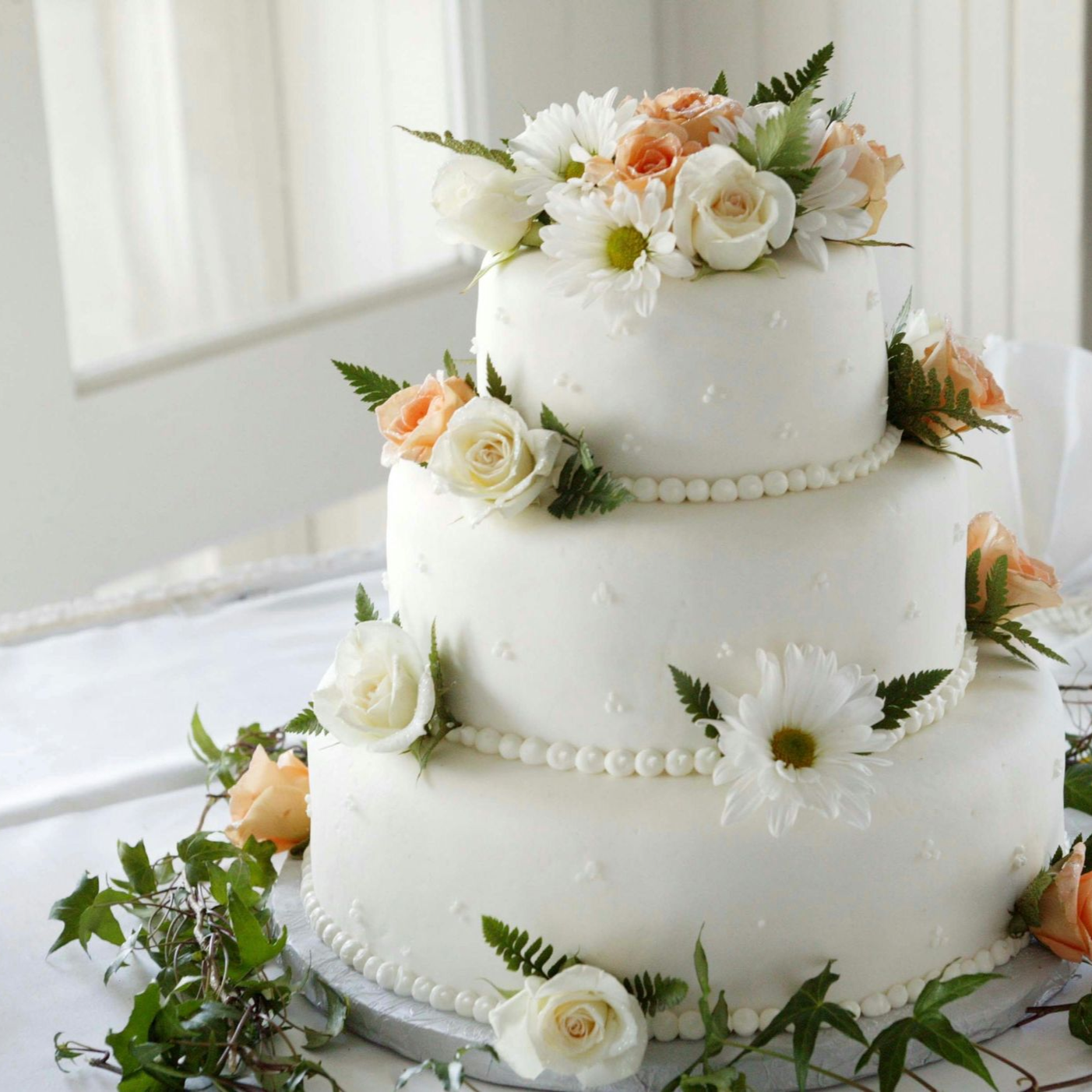Three-tier white wedding cake with white and peach flowers and greenery on a table