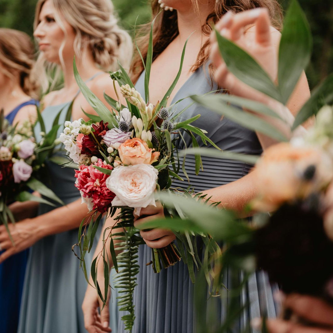 Bridesmaids in blue dresses holding pastel floral bouquets at an outdoor wedding