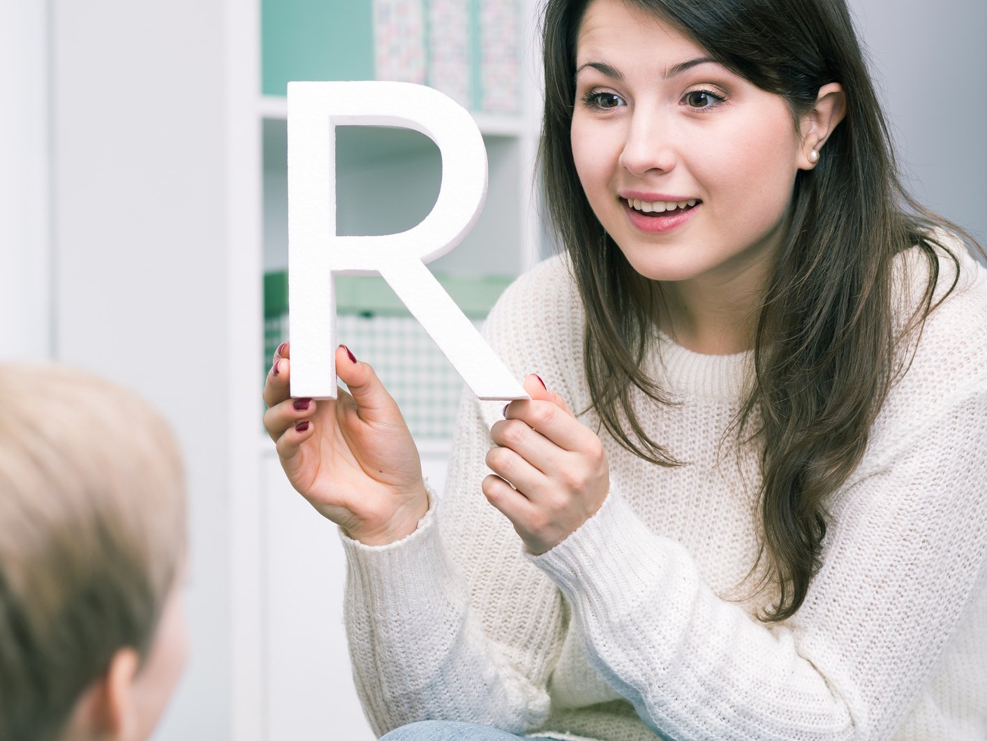 A woman is holding a letter r in front of a child.