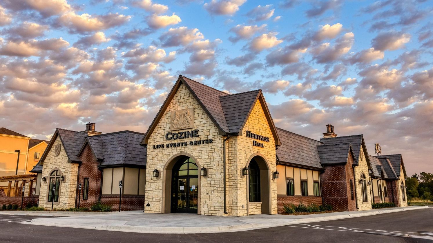 Stone building with arched entrance and sign under a dramatic cloud-filled sunset sky