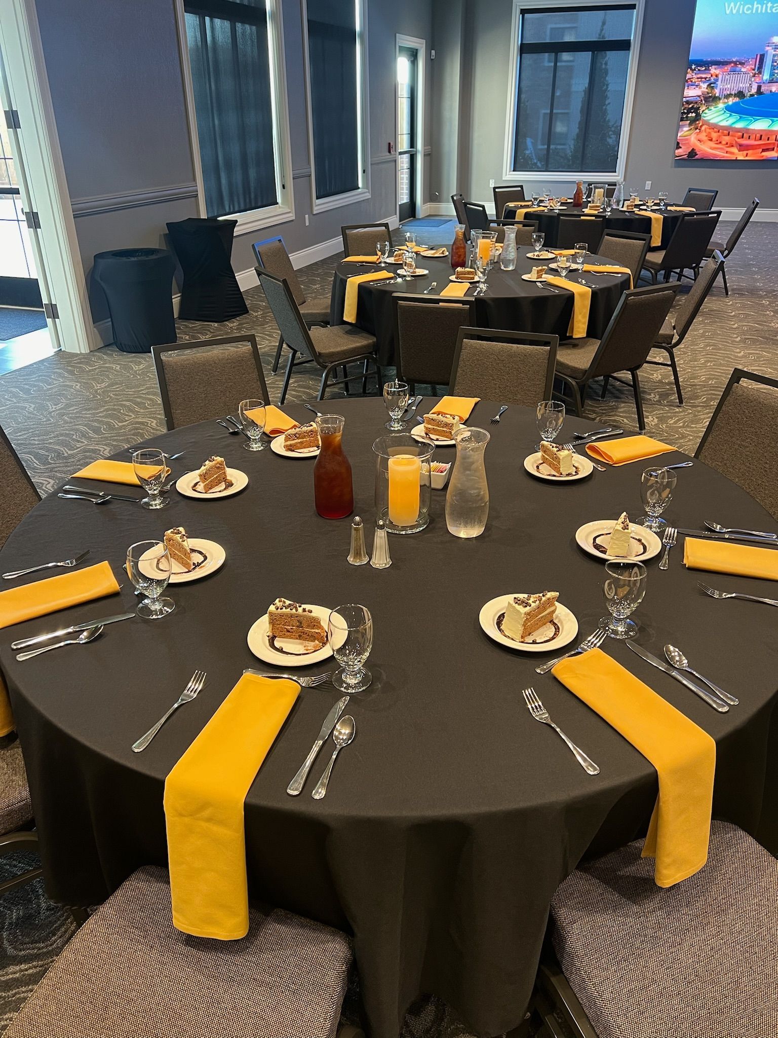 Round banquet table set with black tablecloth, yellow runners, plates, glasses, and condiments in a dining room