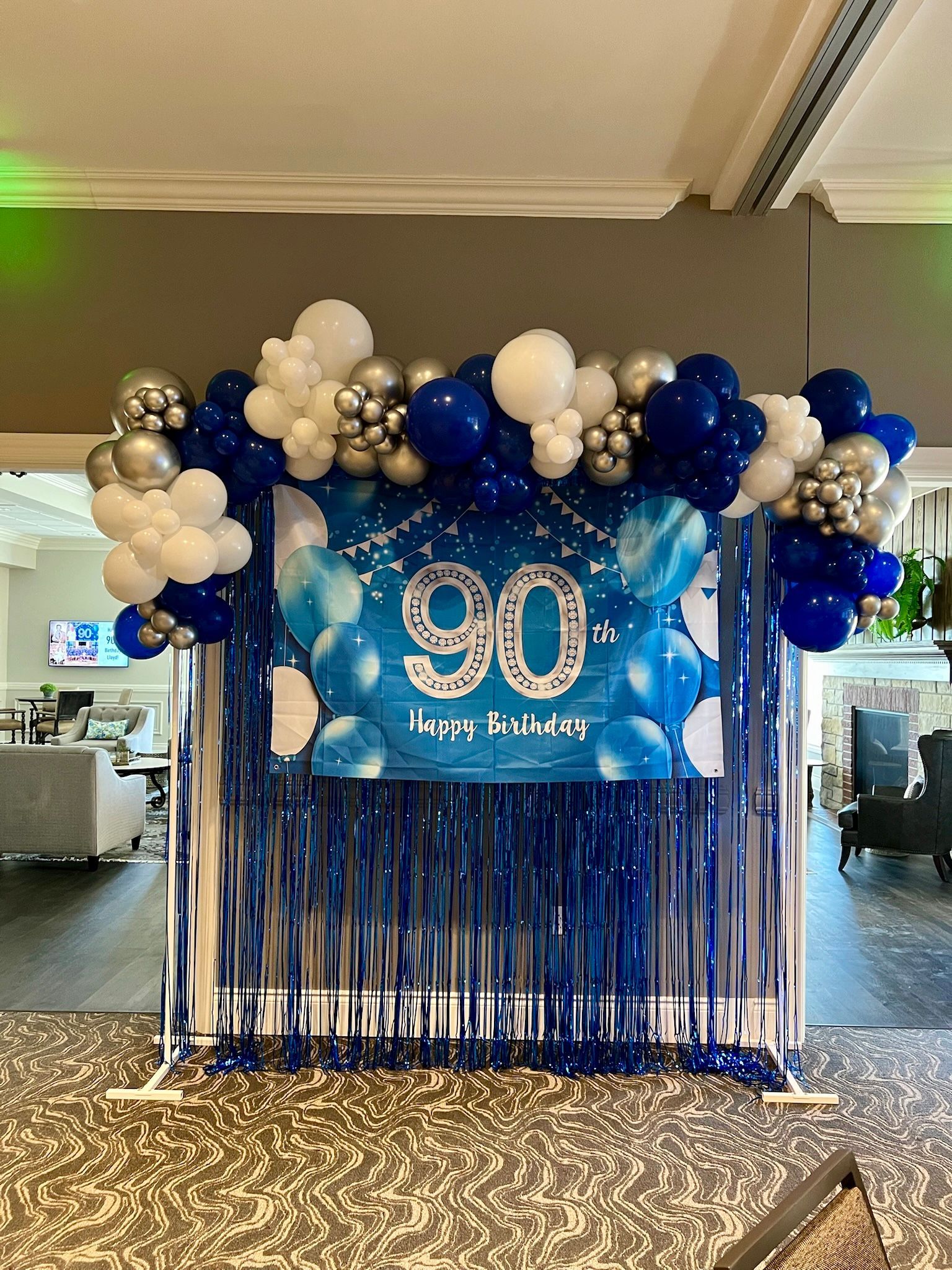 90th birthday balloon backdrop with blue, white, and silver balloons and fringe curtains