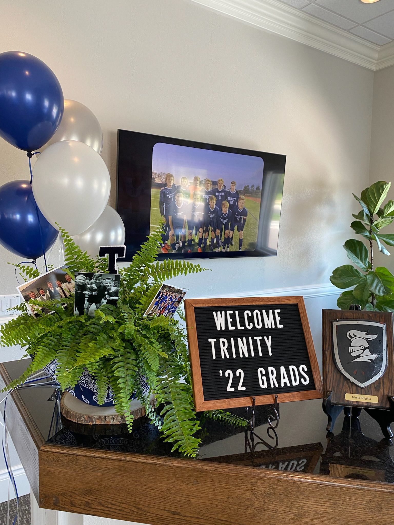Welcome sign for Trinity 2022 grads on a decorated table with balloons, plant, and TV