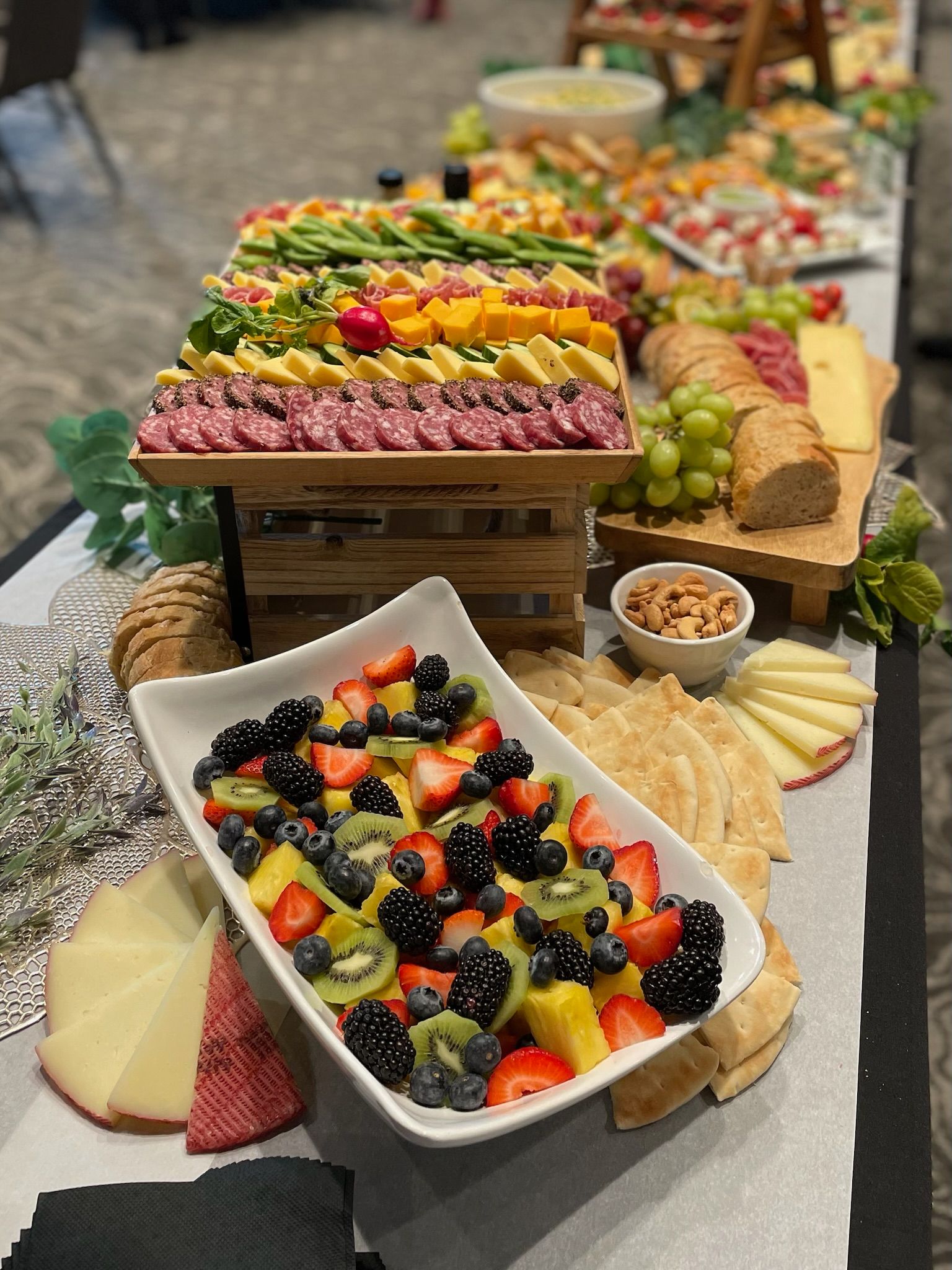 Buffet table with assorted fruit platters, cheeses, grapes, and crackers at an indoor event