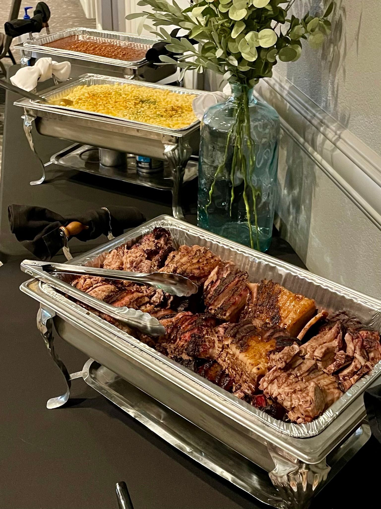 Buffet table with chafing dishes of food beside a vase of white flowers in a formal setting