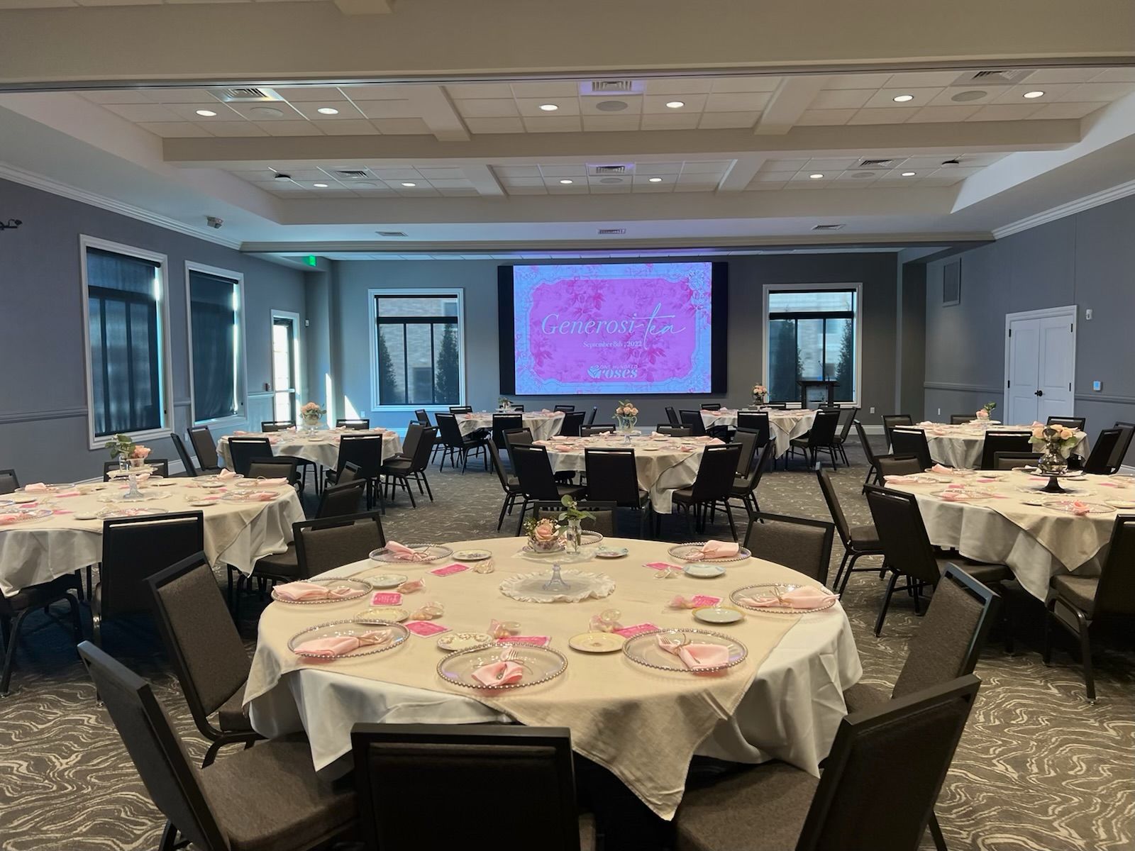 Banquet hall with round tables set for an event and a large presentation screen at the front