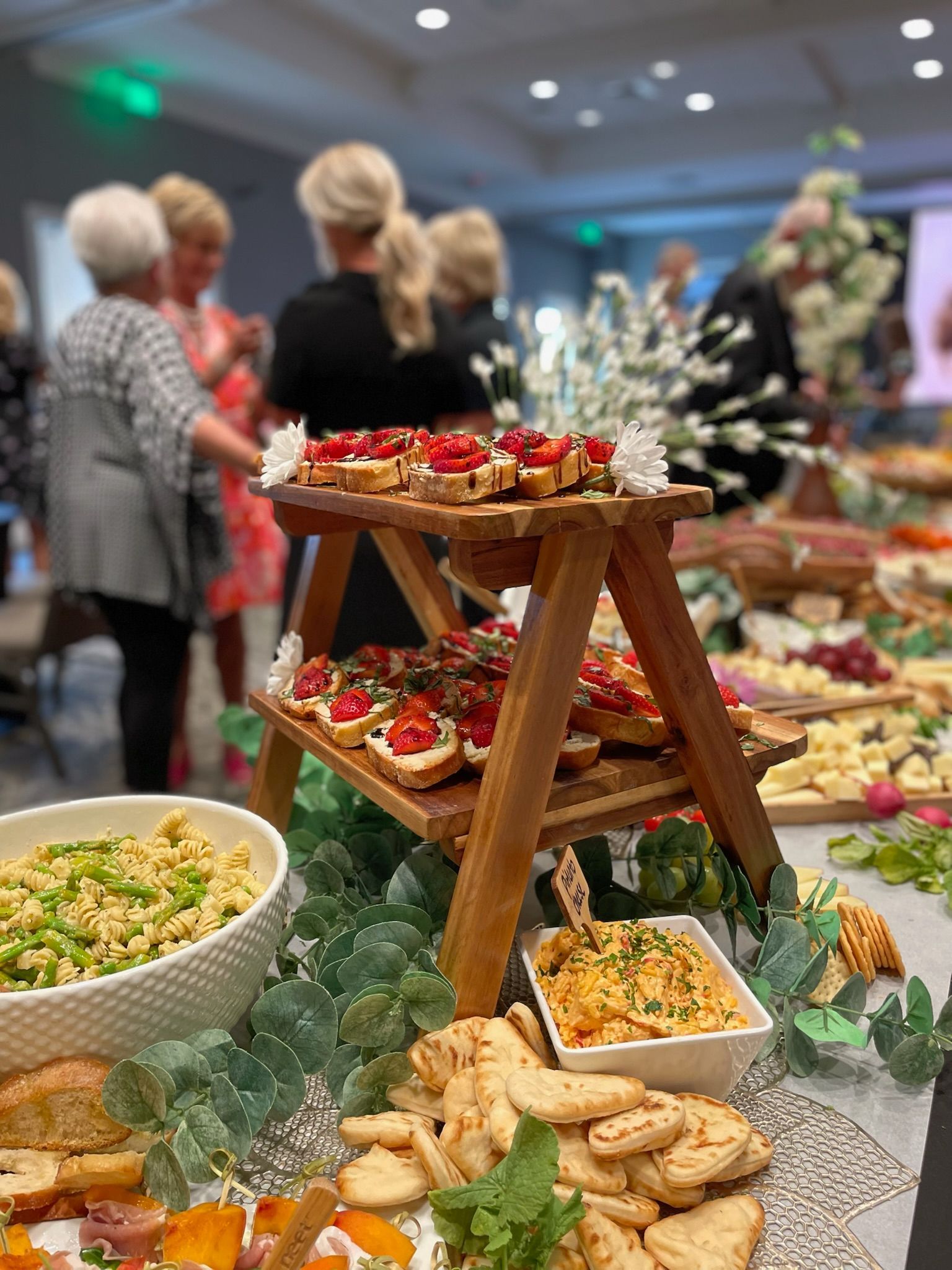 Buffet table with assorted appetizers and desserts at a social event, with guests blurred in the background