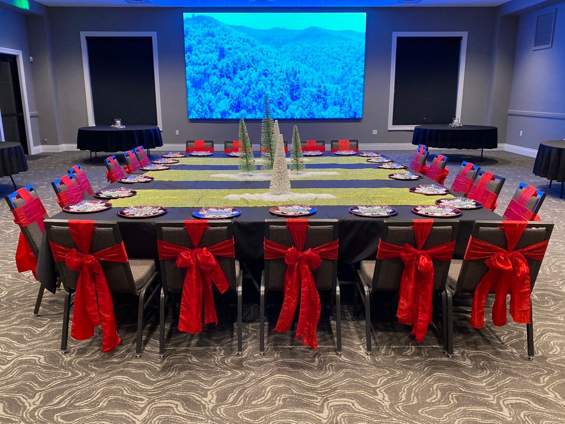 Conference room with U-shaped table, red chair bows, floral centerpieces, and a large blue screen at the front