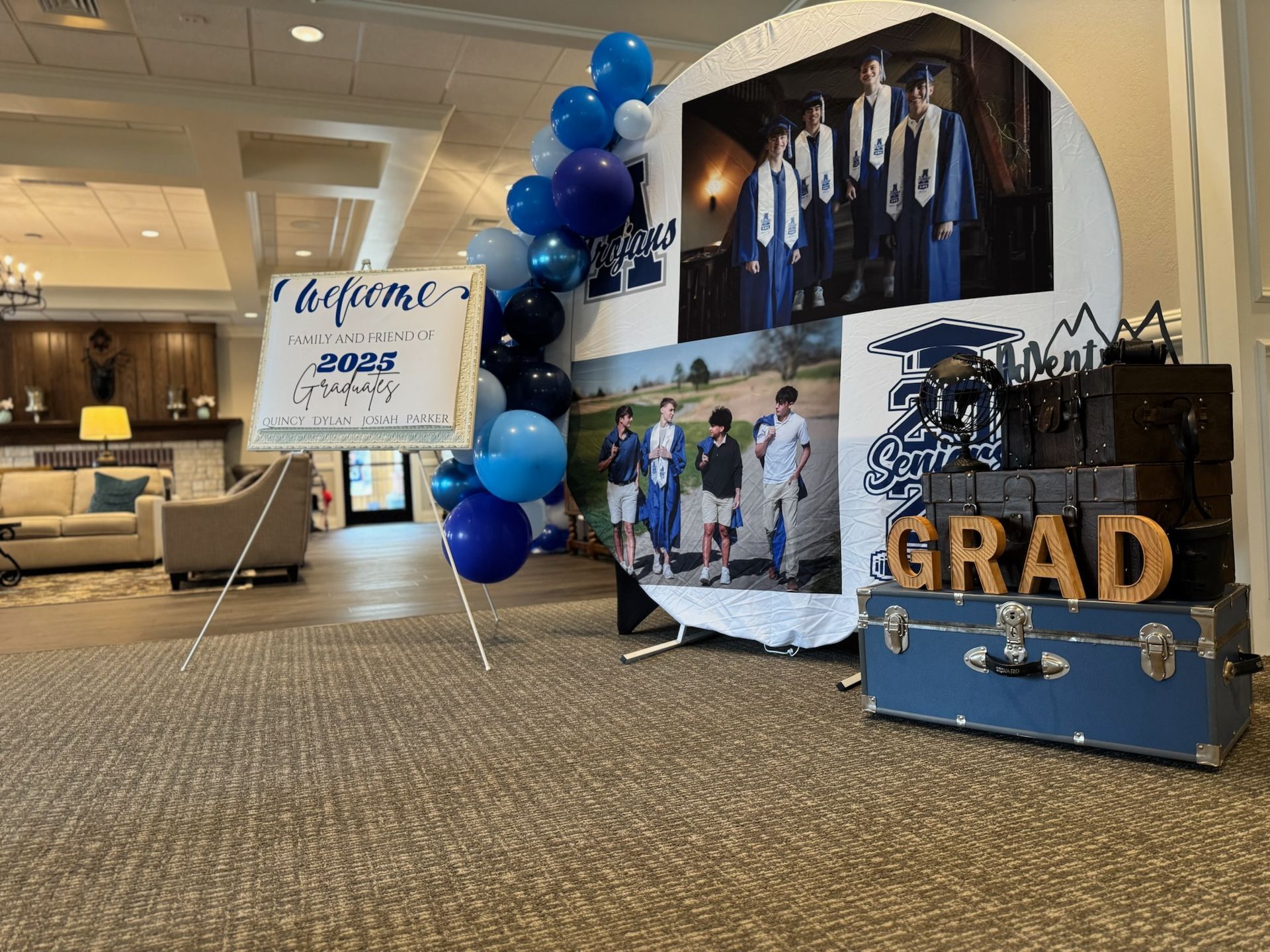 Graduation party display with blue balloons, photo collage, and “GRAD” sign in a lounge lobby
