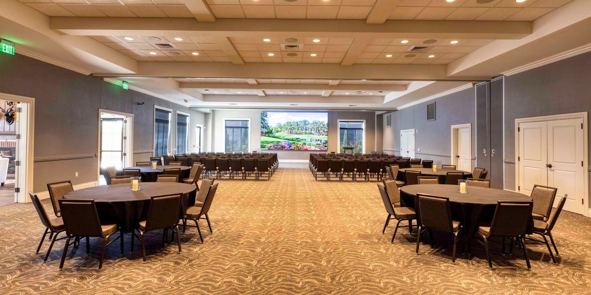 Empty conference room with round tables, chairs, and a large presentation screen at the front