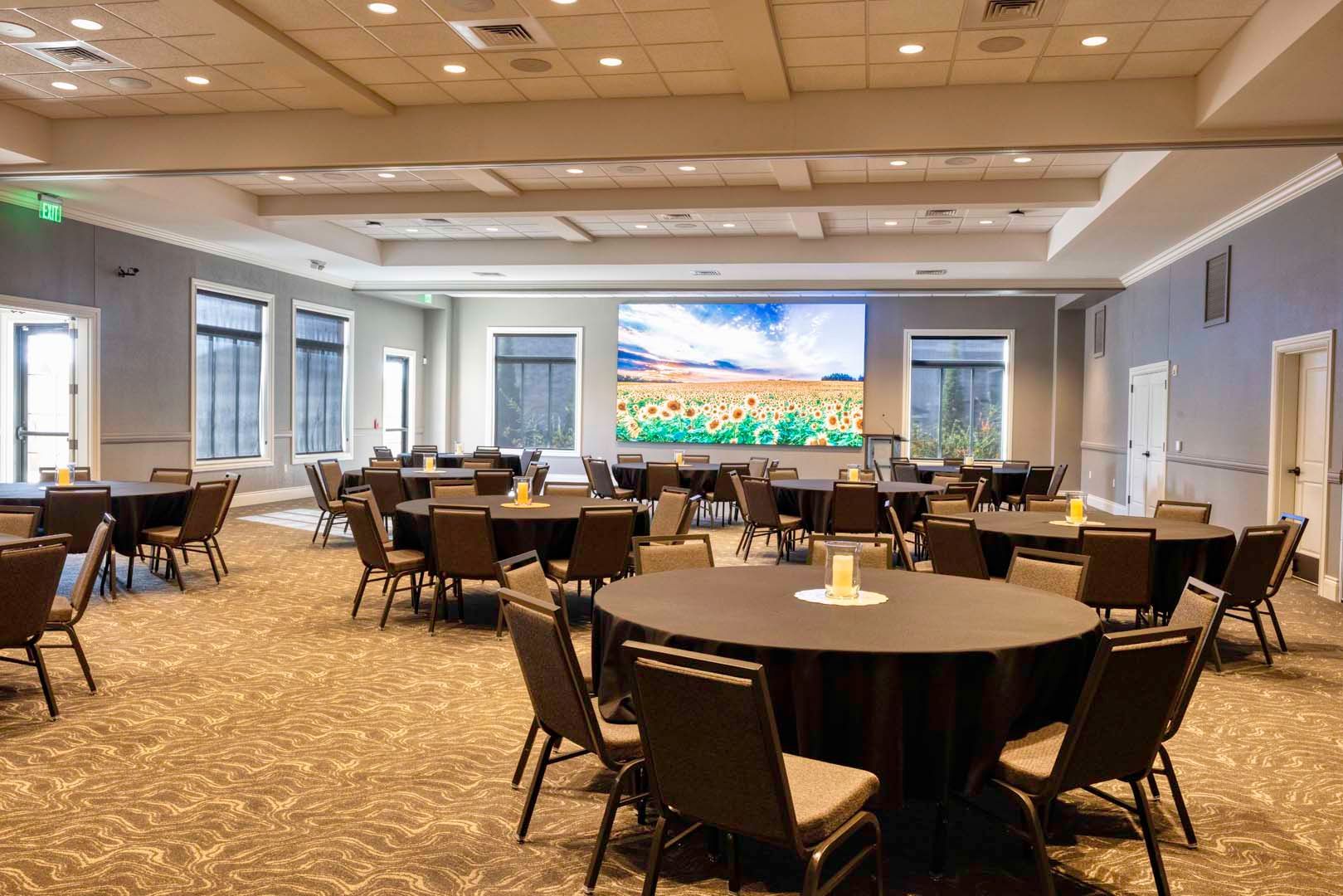 Empty conference room with round tables and chairs, a large presentation screen at the front.