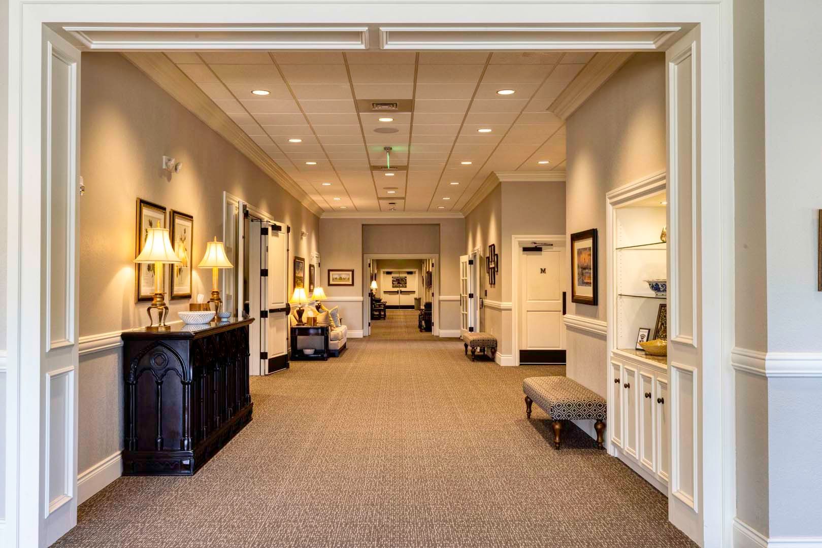 Elegant hotel hallway with carpet, recessed lighting, and decorative tables and artwork