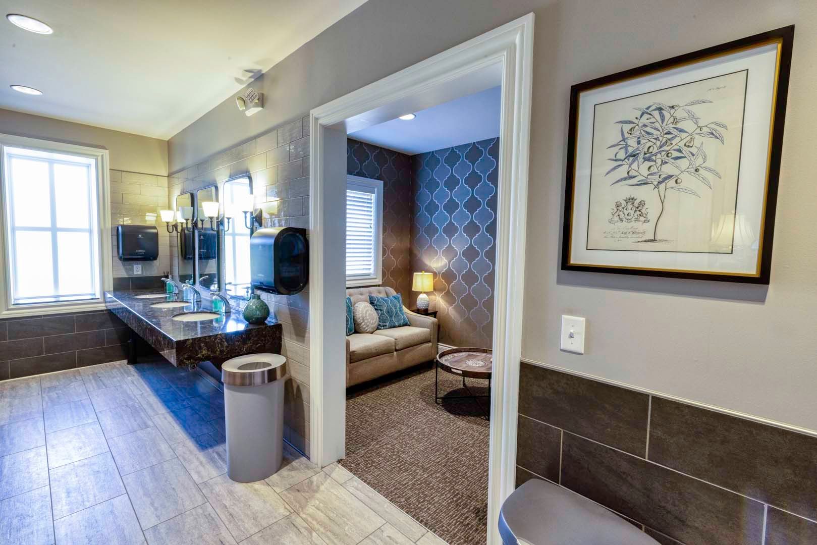 Bright bathroom with a double vanity, tiled floor, and open doorway to a blue-patterned sitting area.
