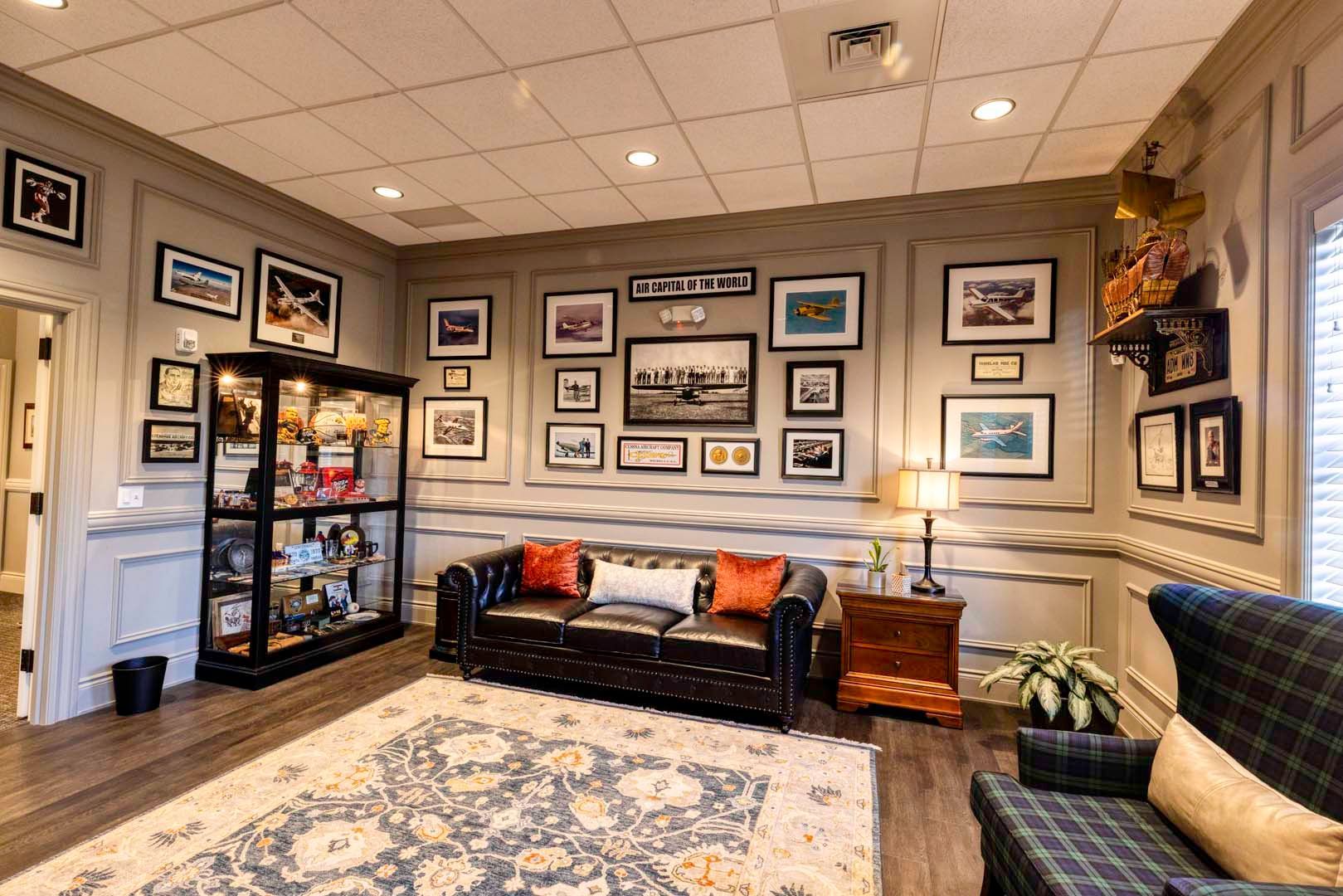 Cozy waiting room with black leather loveseat, framed photos, patterned rug, and wall art