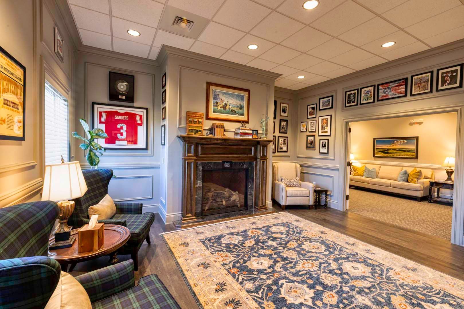 Cozy sitting room with fireplace, plaid chairs, framed art, and blue patterned rug