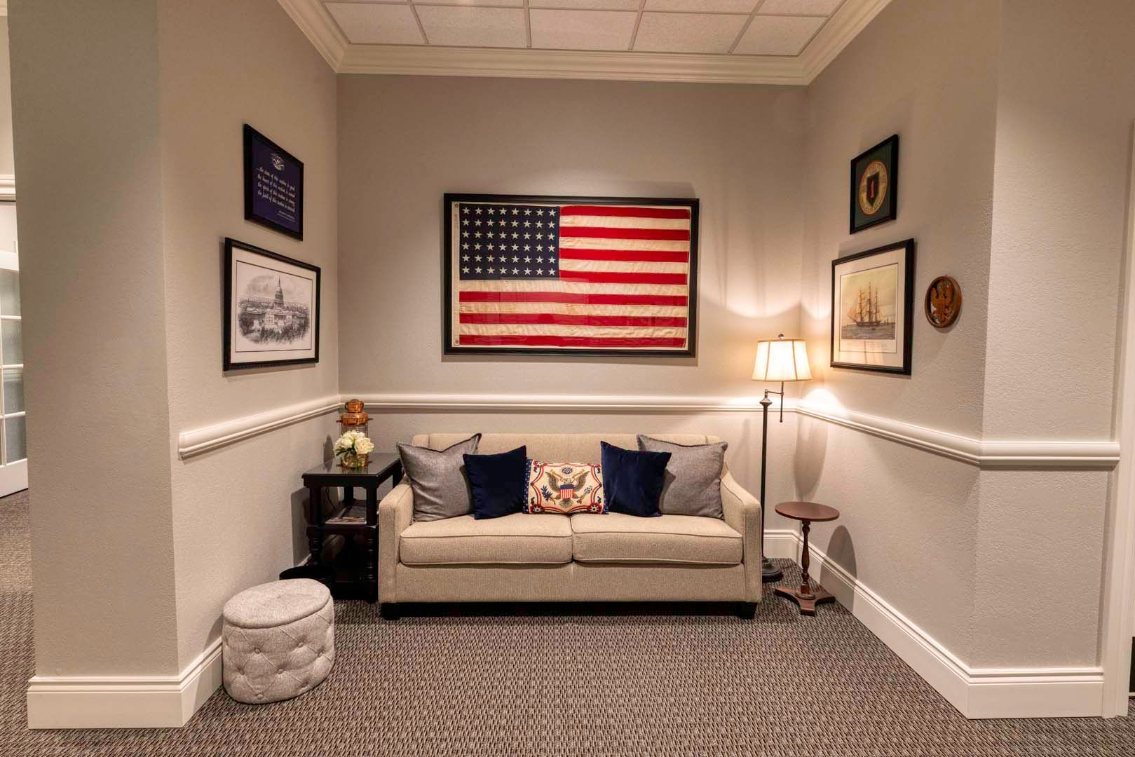 Cozy waiting room with beige couch, lamp, framed art, and large American flag on the wall.