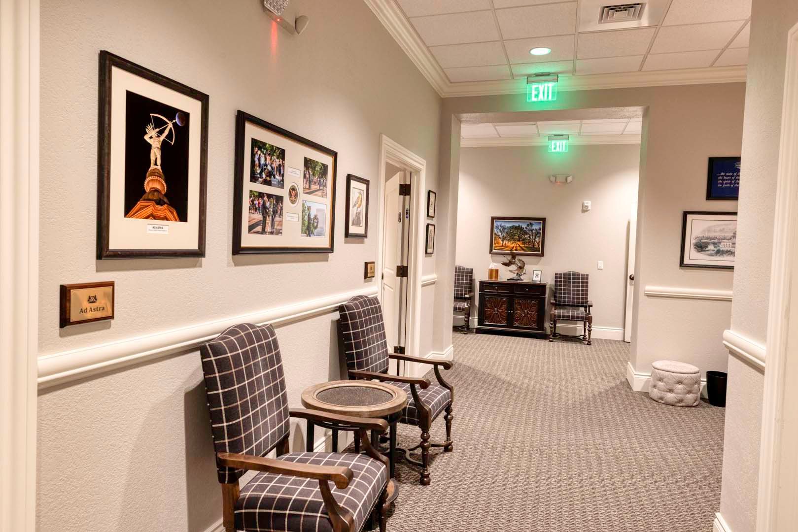 Quiet office hallway with framed art, chairs, and carpeted floor under soft lighting