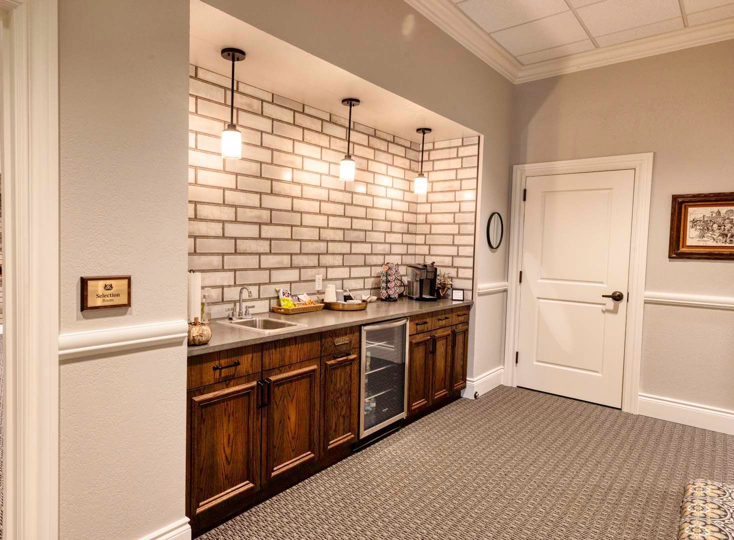Modern kitchenette with wood cabinets, white subway tile backsplash, and pendant lights in a carpeted room