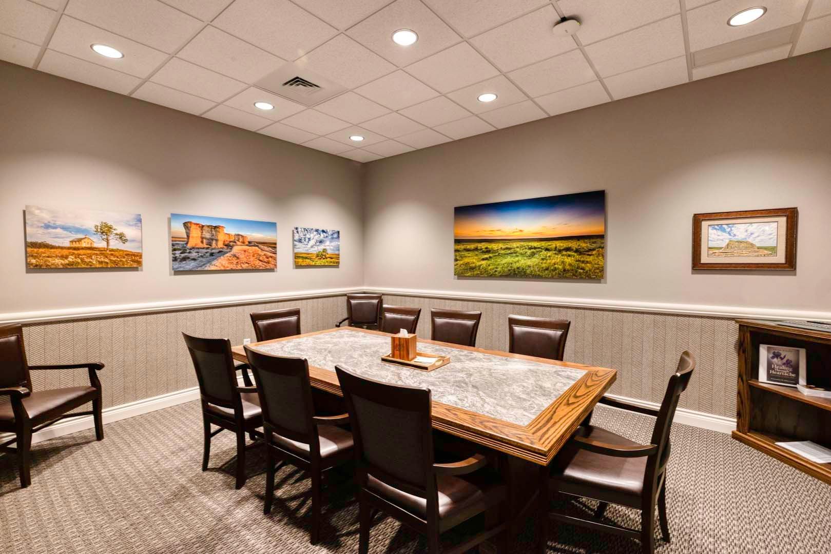Conference room with a wooden table, black chairs, and landscape photos on beige walls.