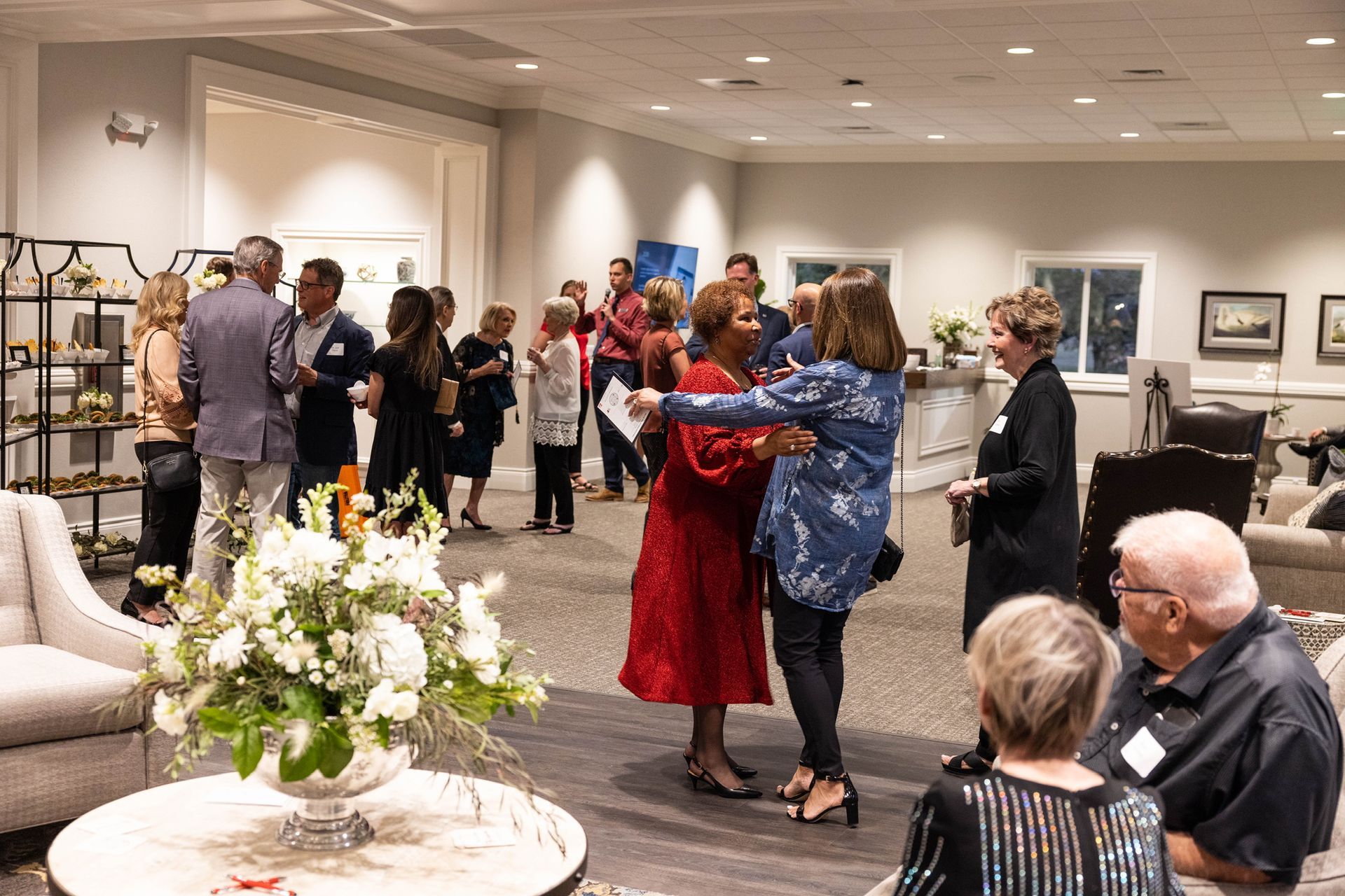 People dancing at a gallery reception, with guests mingling and floral arrangements in the foreground