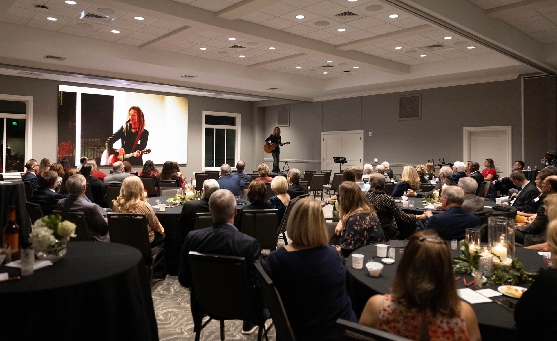 Audience seated in a conference room watching a speaker on a lit stage