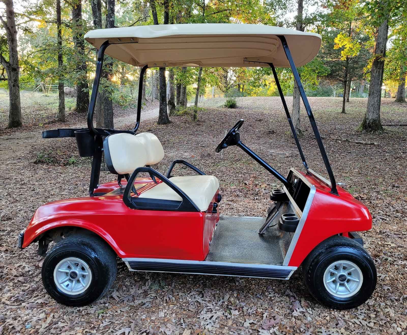 A red golf cart is parked in the middle of a forest.