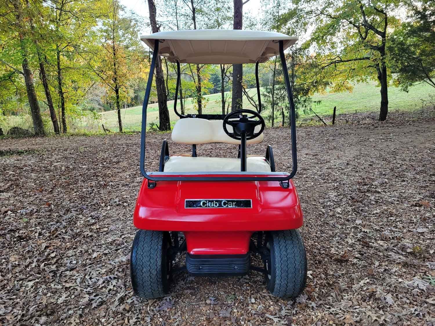 A red golf cart is parked in a pile of leaves.