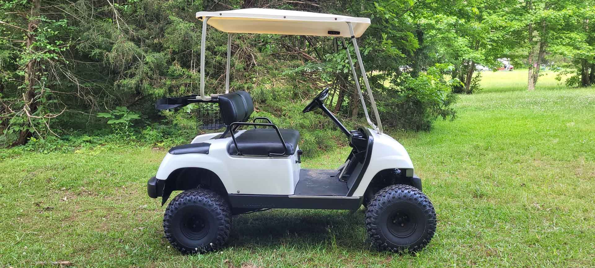 A white golf cart is parked in the grass.