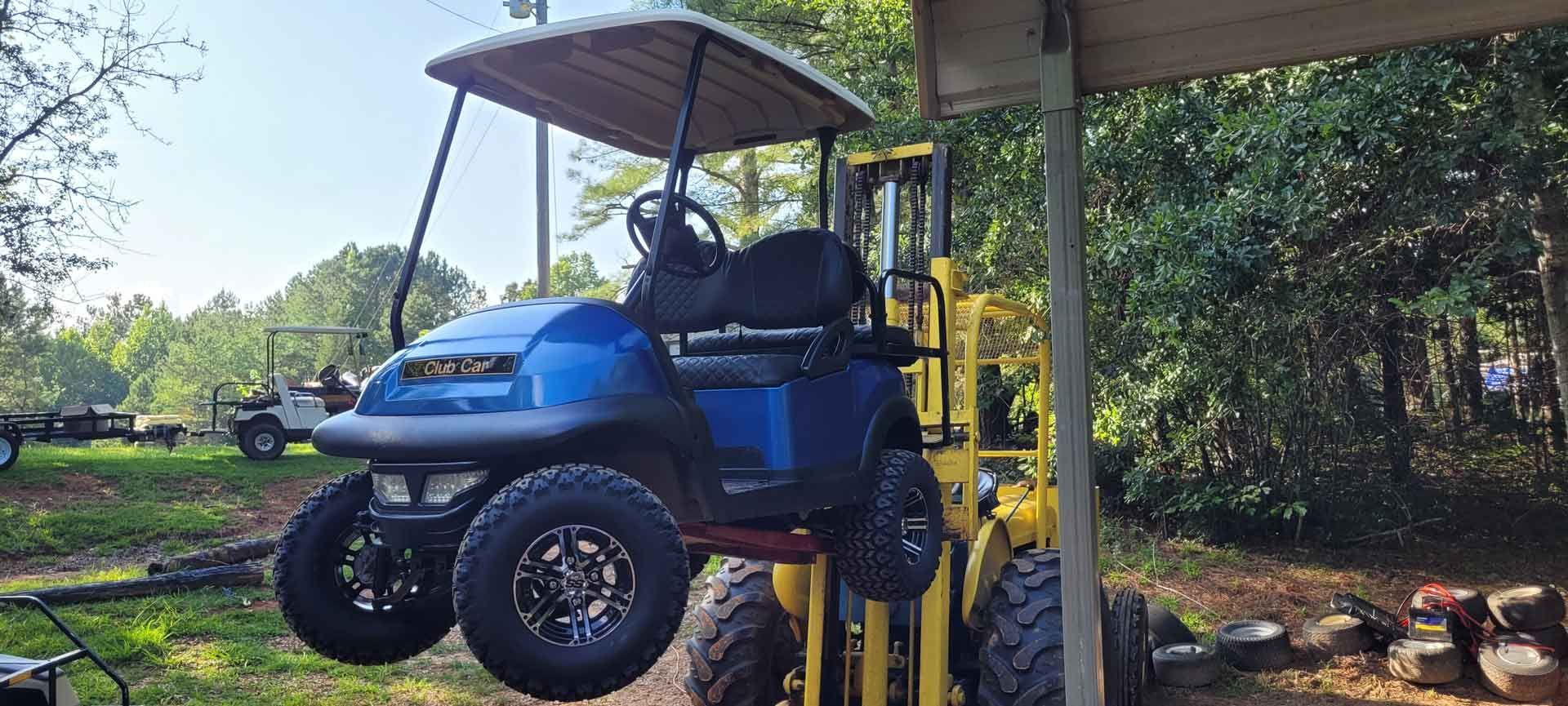 A blue golf cart is being lifted by a forklift.
