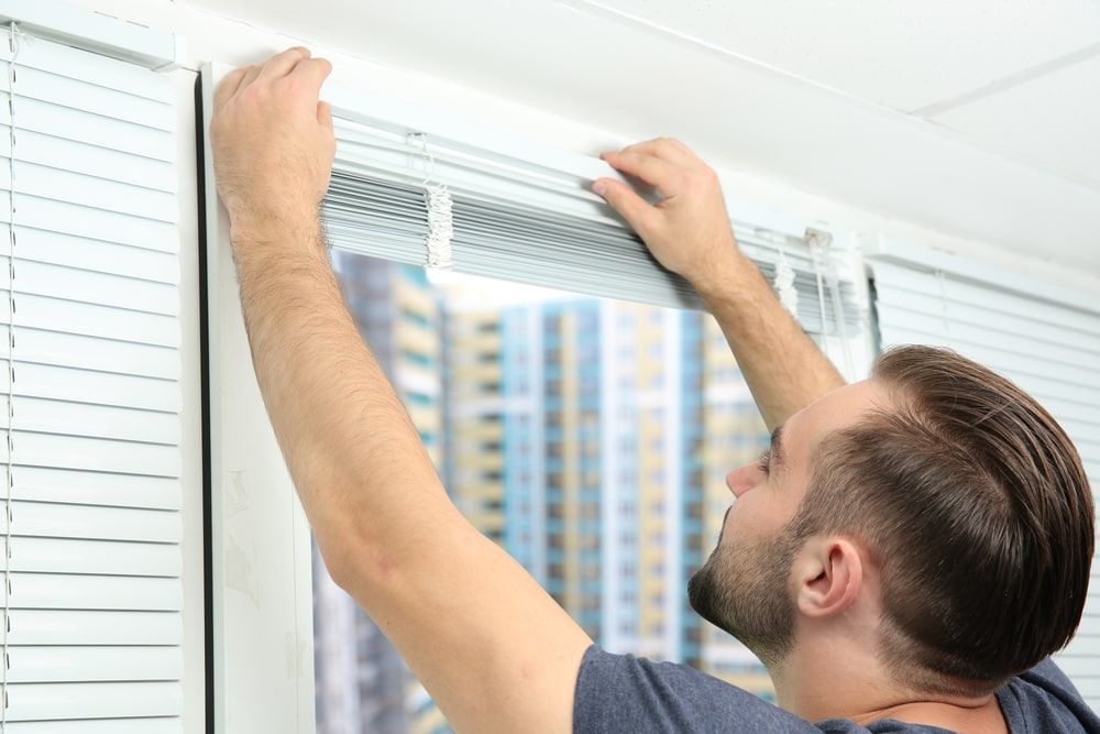 A Man Is Installing Blinds On A Window — Budget Home Improvements In Casuarina, NSW
