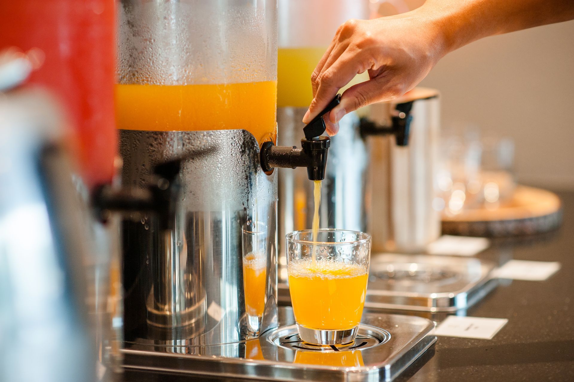 A close-up of a hand pulling down the lever of a juice dispenser for fresh orange juice.