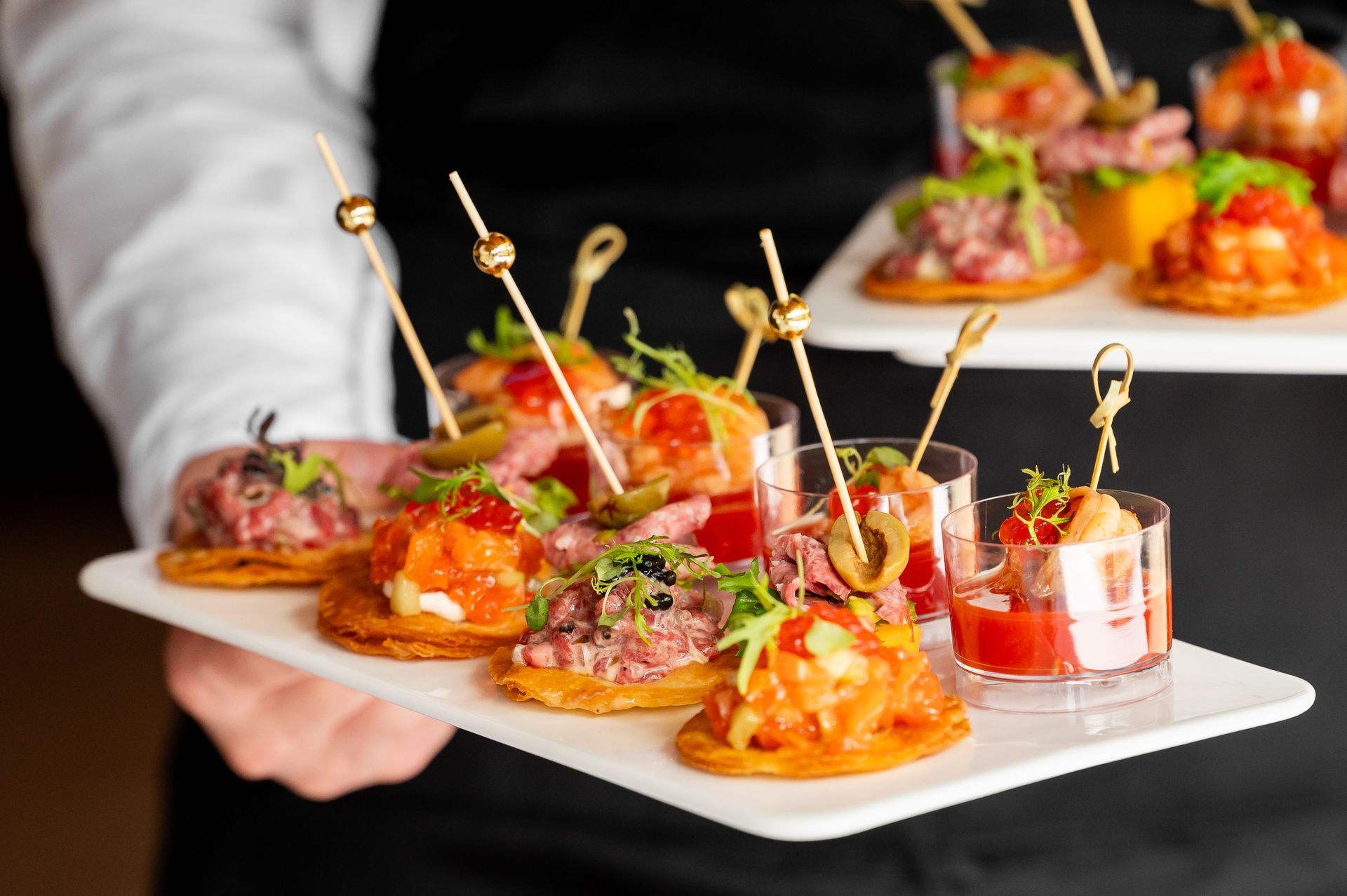 A close-up of a waiter with a tray filled with various appetisers