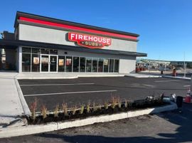 Firehouse Subs storefront with large red sign, parking lot, and clear blue sky