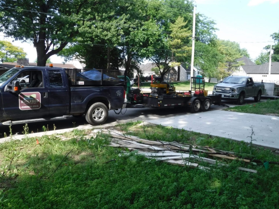 Black pickup truck towing a flatbed trailer with a silver car parked on a tree-lined residential street.