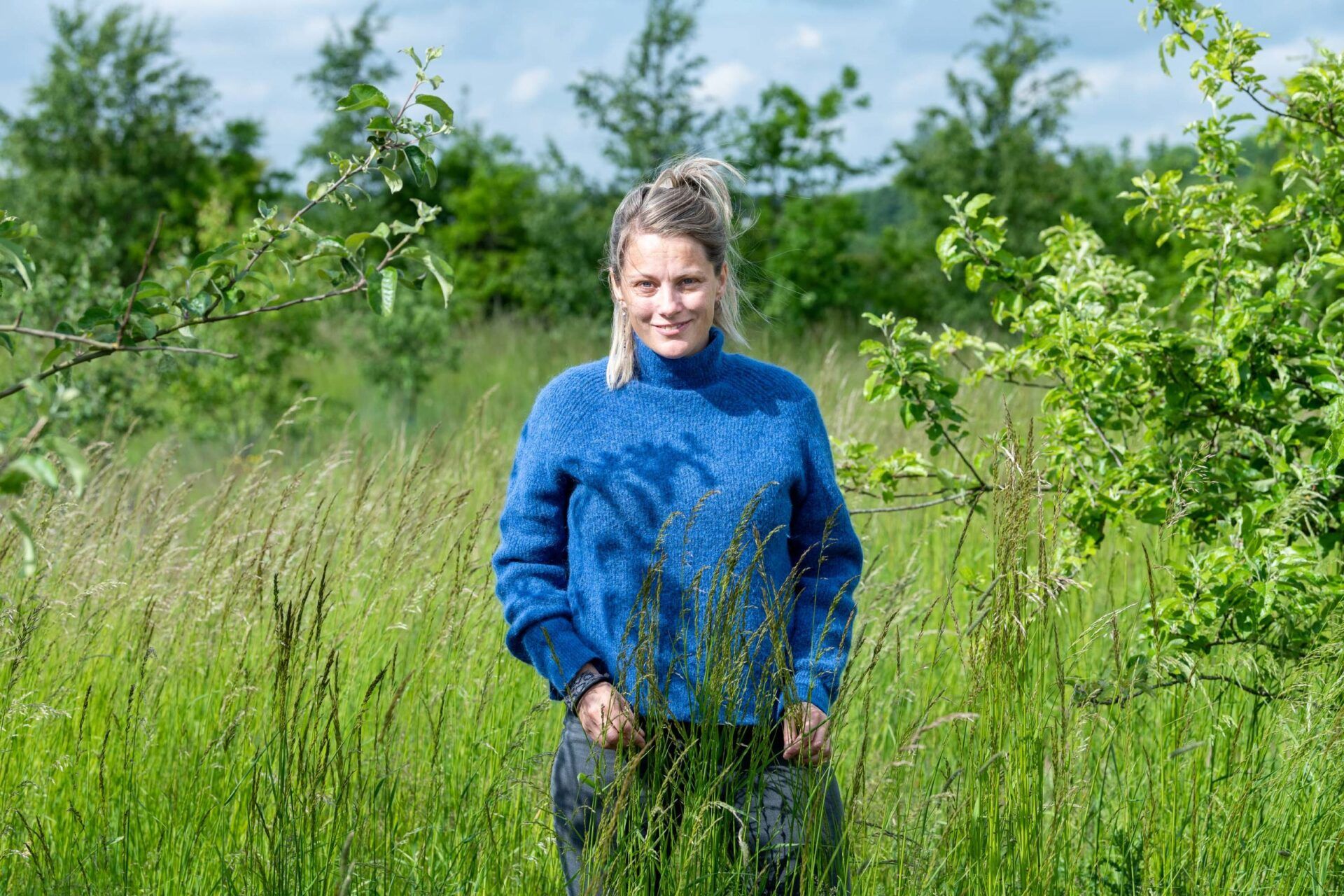 Psykolog Louise Søndergaard i en blå sweater står på en græsmark.