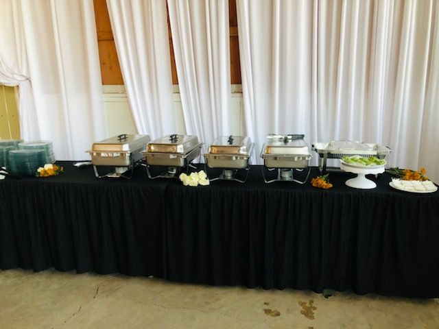 A buffet table with a black table cloth and a white curtain behind it