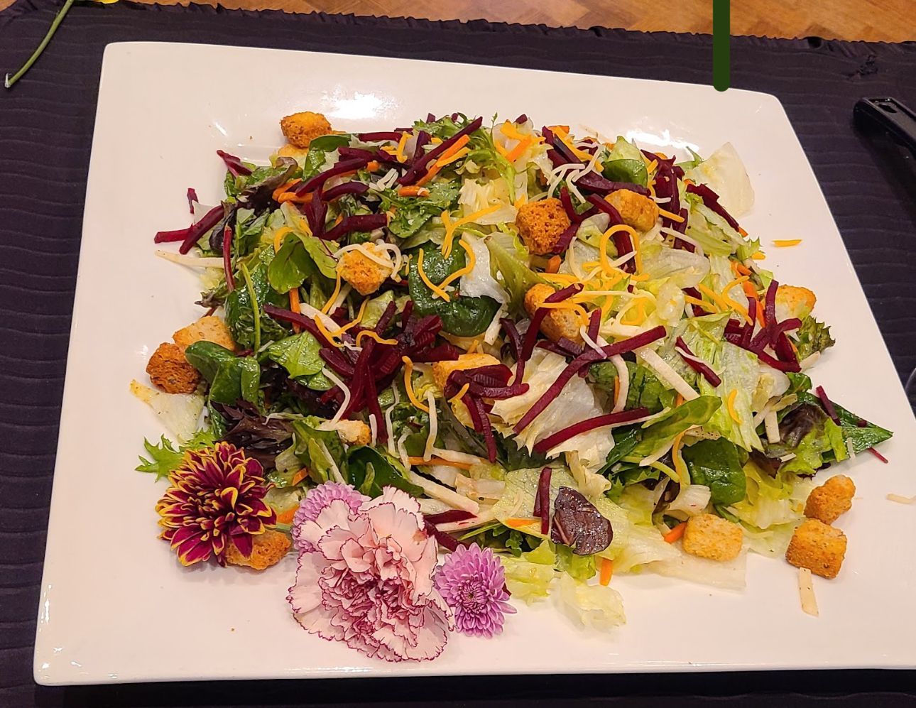A salad with croutons and flowers on a white plate