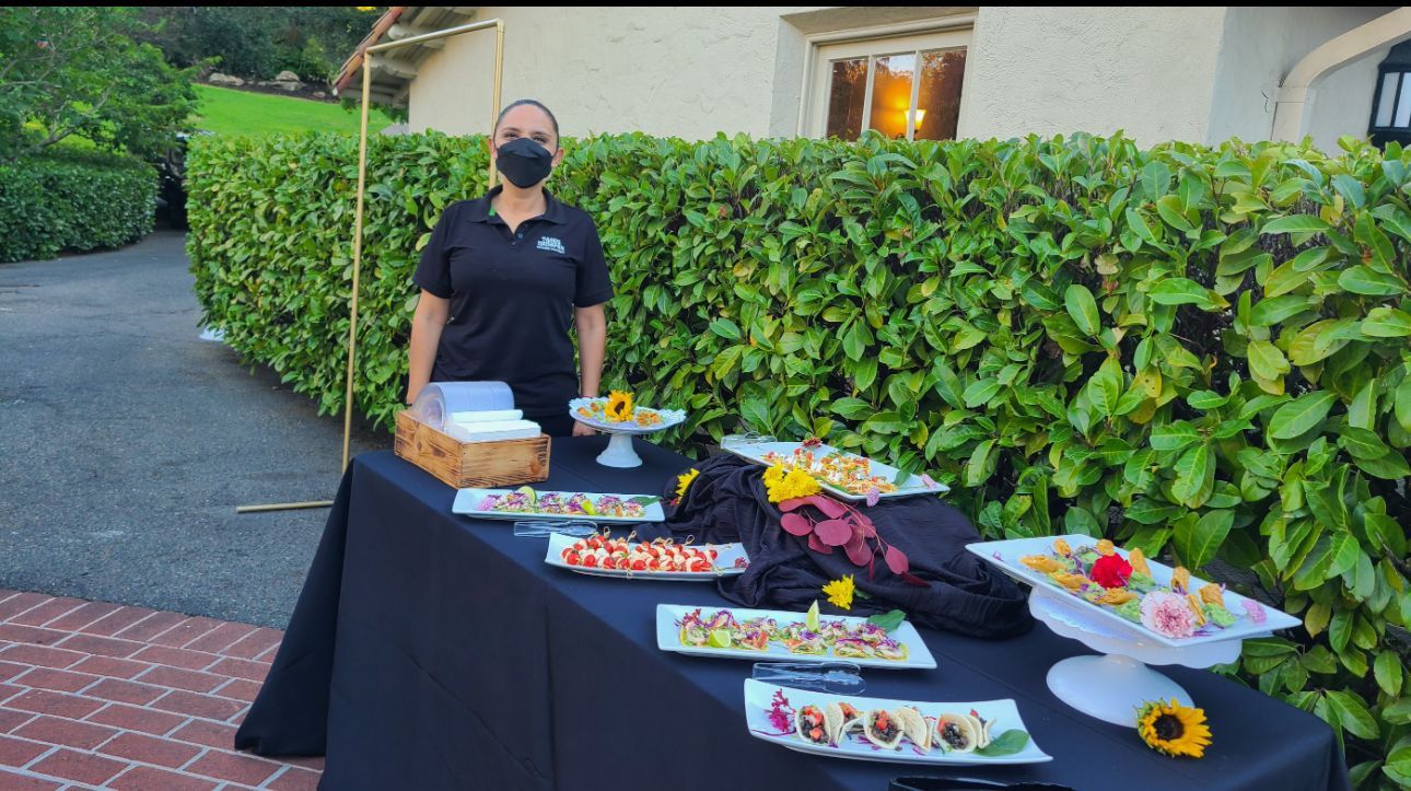 Diana wearing a mask is standing in front of a table with food on it.