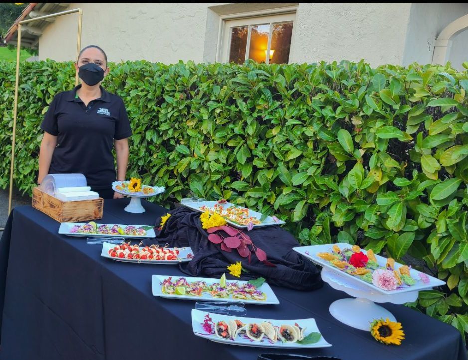 A woman wearing a mask is standing in front of a table with food on it.