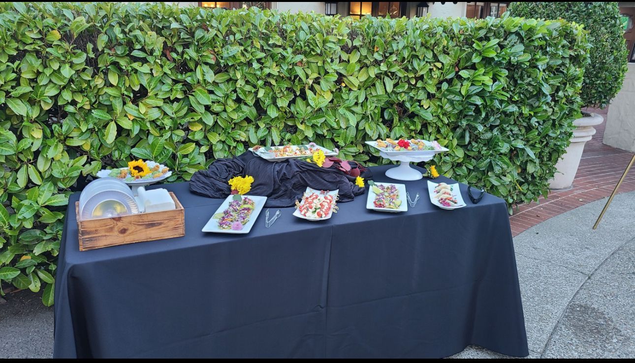 A table with plates of food on it is sitting in front of a hedge.