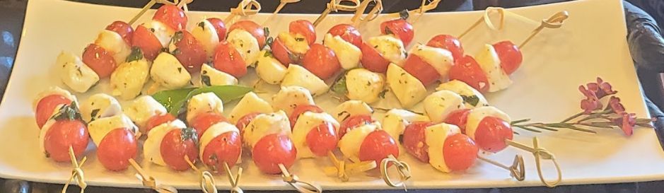 A white plate topped with tomatoes and cheese on skewers.